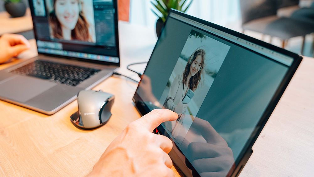 laptop connected to a portable monitor with a hand touching the screen.