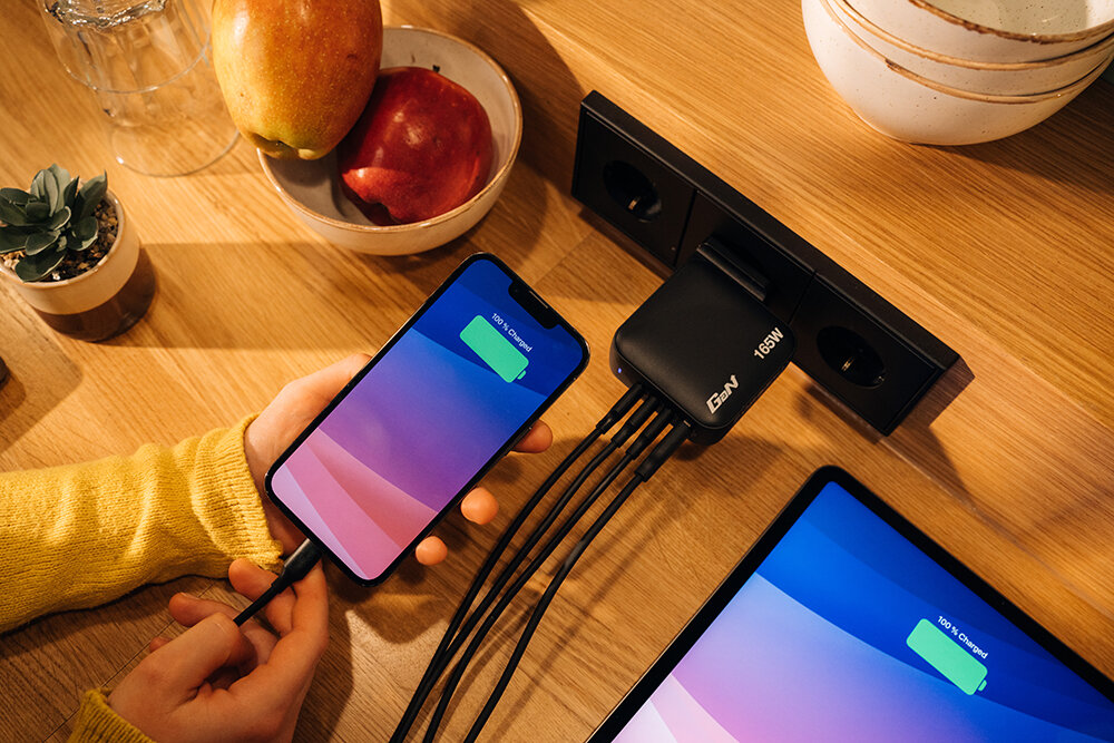GaN Charger with 4 cables plugged into it, charging a phone and iPad to 100% charged.
