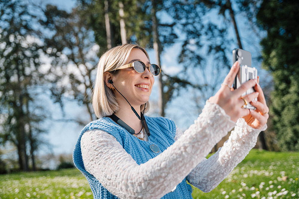 Spring solutions_woman outside in the sunshine with earbuds and phone attached to a powerbank