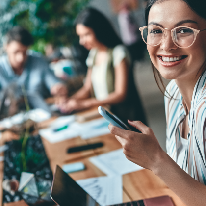 Žena koja se smiješi s telefonom u ruci ispred prijenosnog računala.