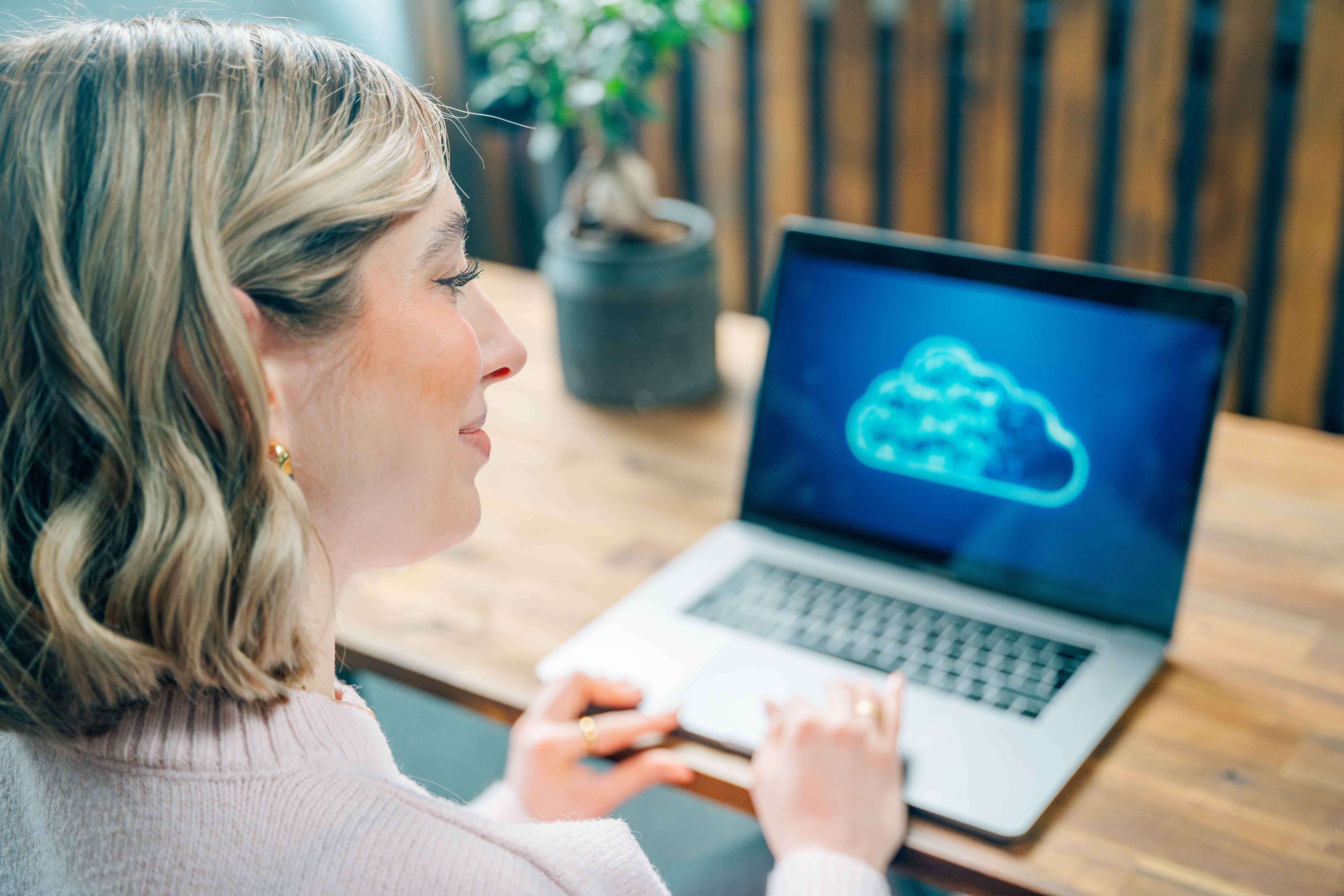 En kvinna vid ett skrivbord med en bärbar dator som gör en säkerhetskopiering till molnet