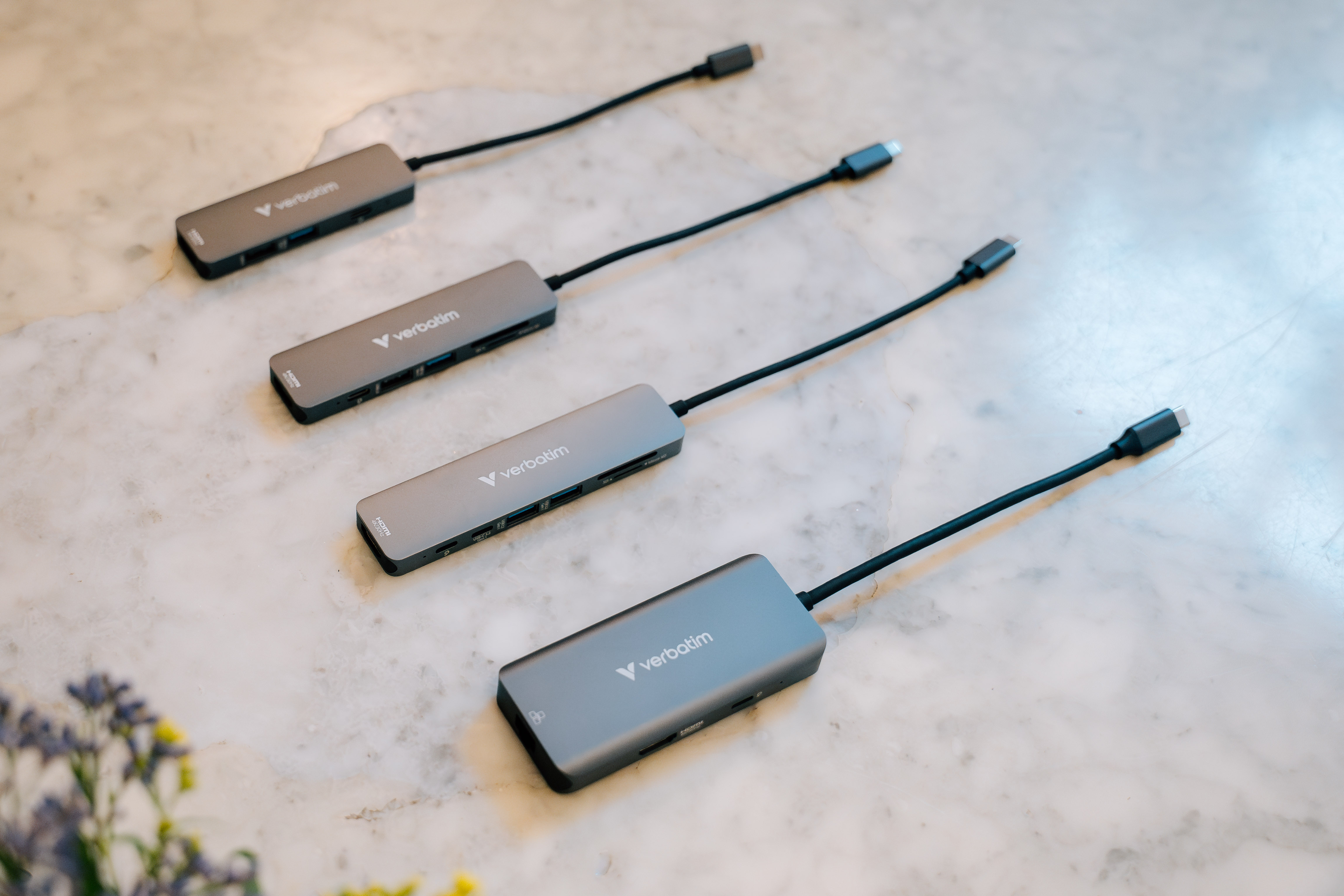 Vier silberne Verbatim USB-C-Hubs auf einer Marmorarbeitsplatte.